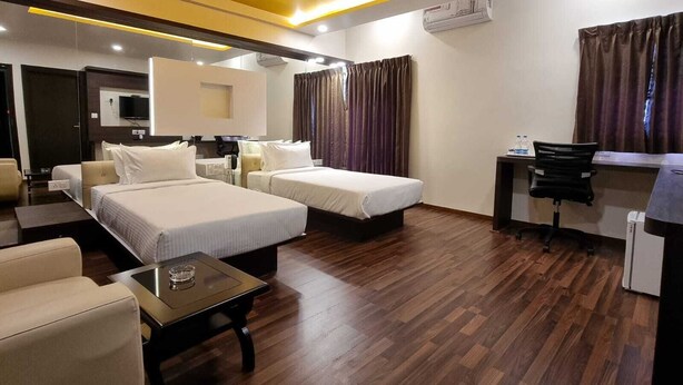 A hotel room with two beds, a desk, a chair, a small table, and an air conditioning unit. - VN Alpha Suites (Bengaluru)