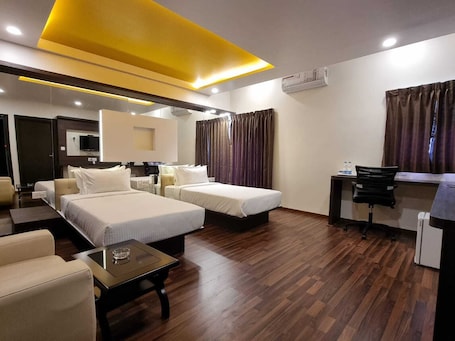 A hotel room with two beds, a desk, a chair, a small table, and an air conditioning unit.