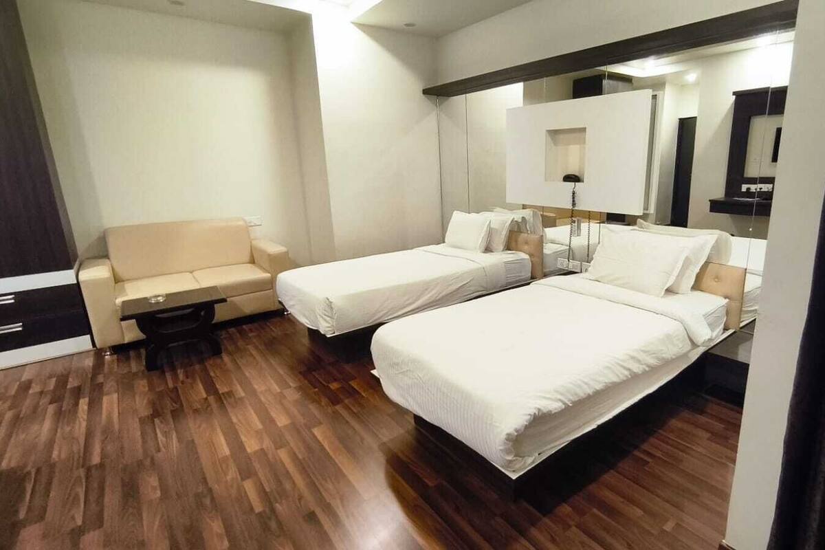 A hotel room with two beds, a sofa, a bedside table, a mirror, and a wooden floor.