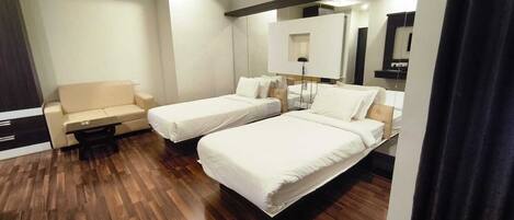 A hotel room with two beds, a sofa, a bedside table, a mirror, and a wooden floor.