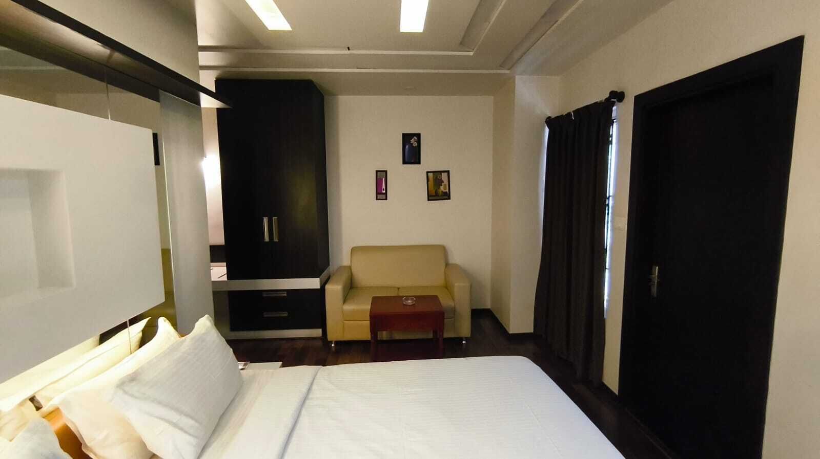 A hotel room with a bed, a sofa, a small table, a wardrobe, and a wall with pictures.