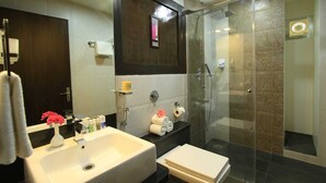 A modern bathroom with a large sink, a toilet, a glass-enclosed shower, and a dark wooden vanity. - VN Alpha Suites (Bengaluru)