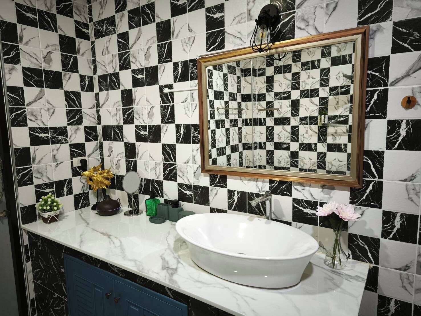 A bathroom with a checkered black and white tile backsplash, a white sink, and a mirror with a wooden frame.