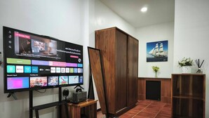 Olohuoneessa on litteänäyttöinen televisio, jolla näkyy useita suoratoistopalveluita, puinen kaappi, seinällä oleva kehystetty kuva ja laatoitettu lattia.