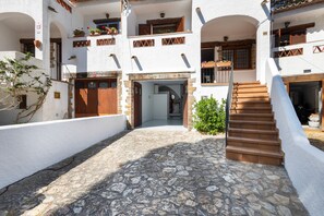 Un patio con suelo de piedra, una escalera y edificios blancos con balcones de madera.