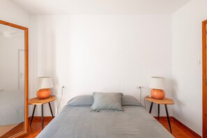 Un dormitorio con una cama, dos mesitas de noche con lámparas, un espejo y una puerta.