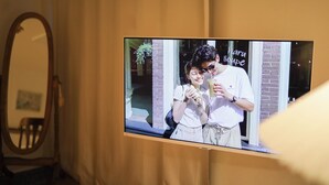 En tv-skärm som hänger på väggen och visar ett par som håller i varsin drink.
