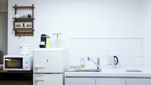 Ett kök med mikrovågsugn, kaffebryggare, vattenkokare och en hylla med köksutrustning.