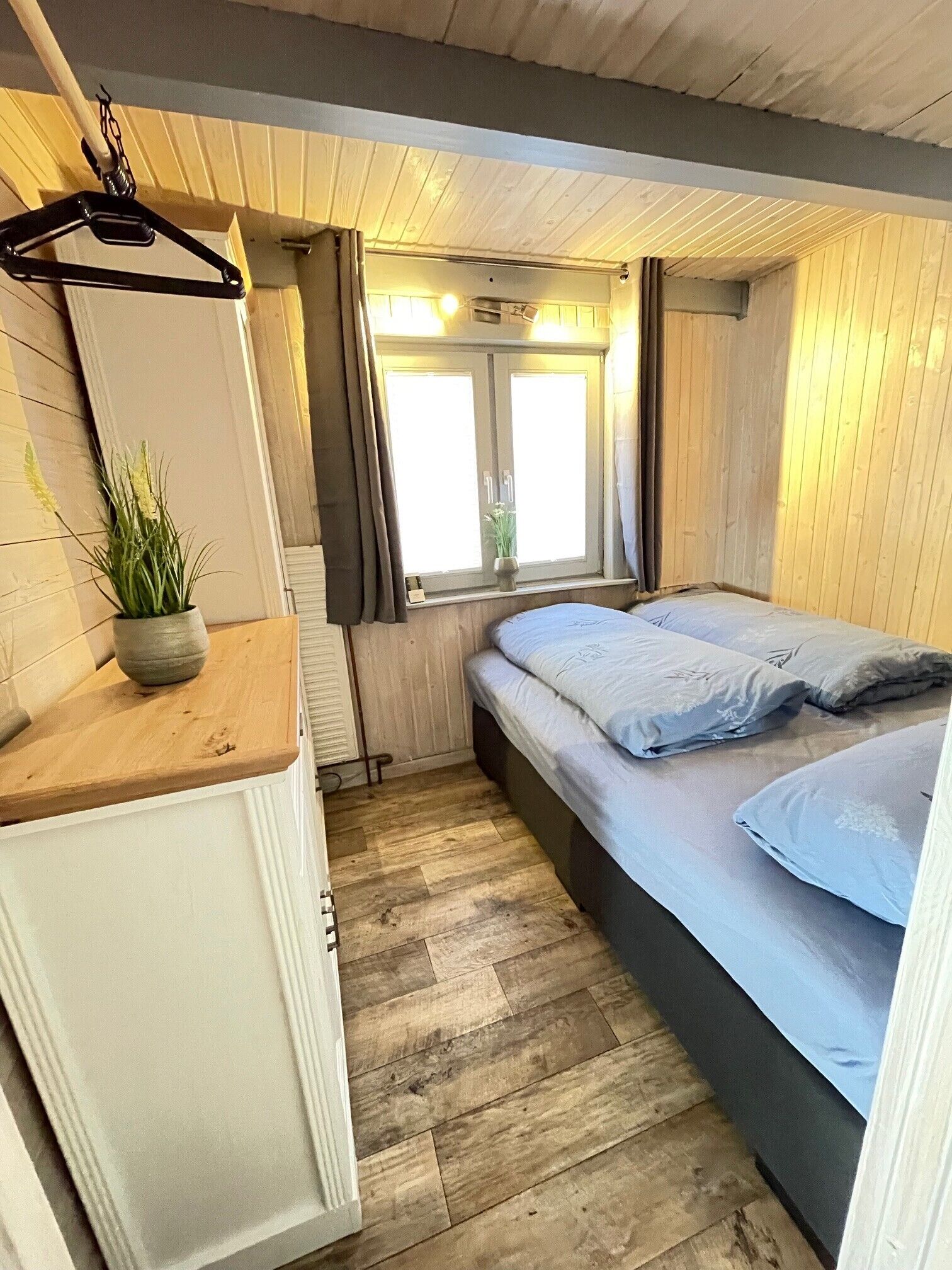 Ein gemütlicher Raum mit Bett, kleinem Tisch, Heizkörper und einem Fenster mit Vorhängen.
