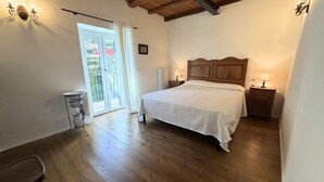 A bedroom with a wooden floor, a bed with a white bedspread, a nightstand with a lamp, and a window with curtains. - Enchantment of the Lake - app Cernobbio Two-room apartment with A / C (Molina)