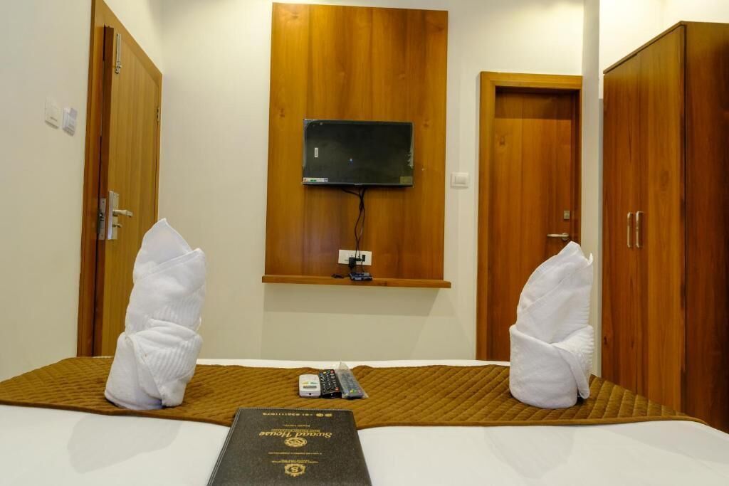 A hotel room with a bed, a TV mounted on the wall, wooden wardrobes, and towels on the bed.
