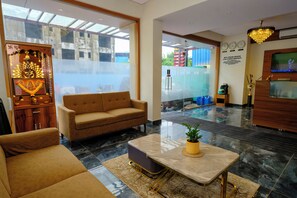 A modern hotel lobby with a sofa, a coffee table, a reception desk, and a television. - Hotel Sterling Executive (Navi Mumbai)