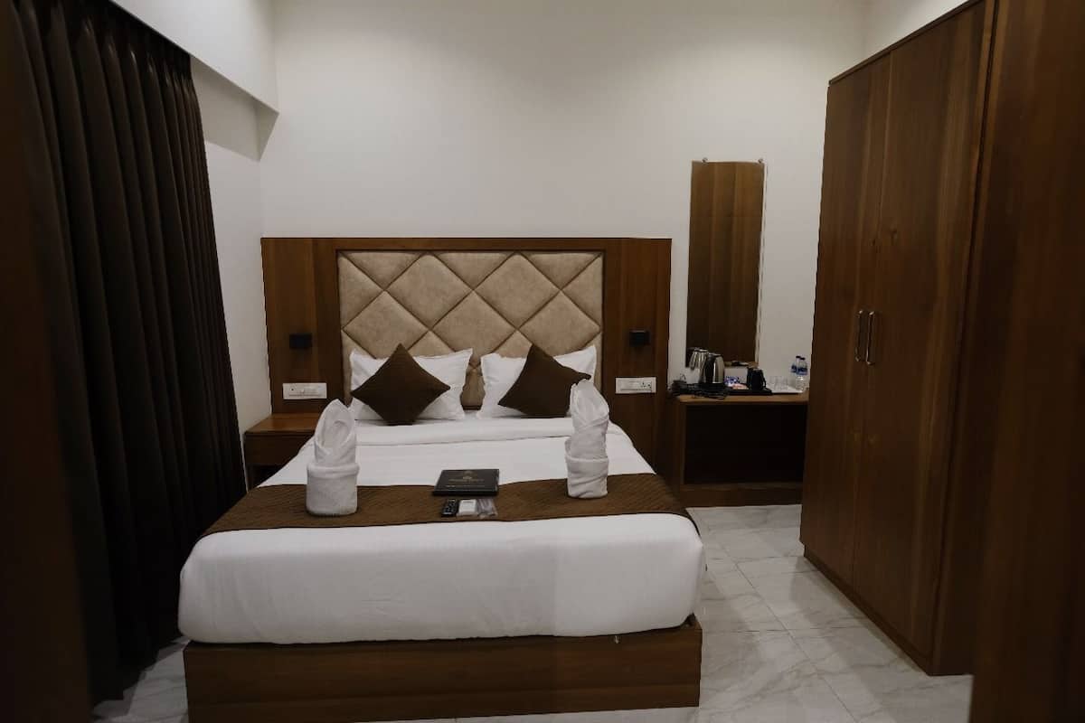 Quarto de hotel com cama, cabeceira de madeira, mesa de cabeceira, guarda-roupa e espelho.