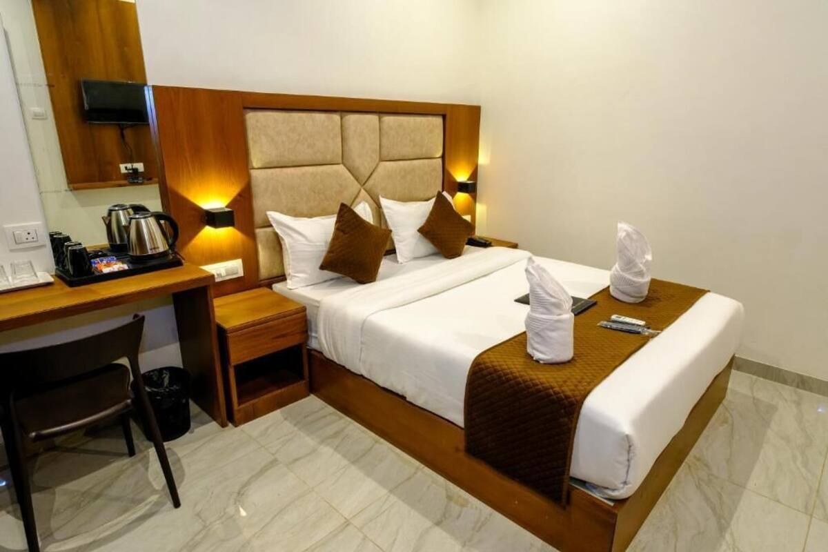 Quarto de hotel com cama, mesas de cabeceira, escrivaninha, cadeira e televisão.