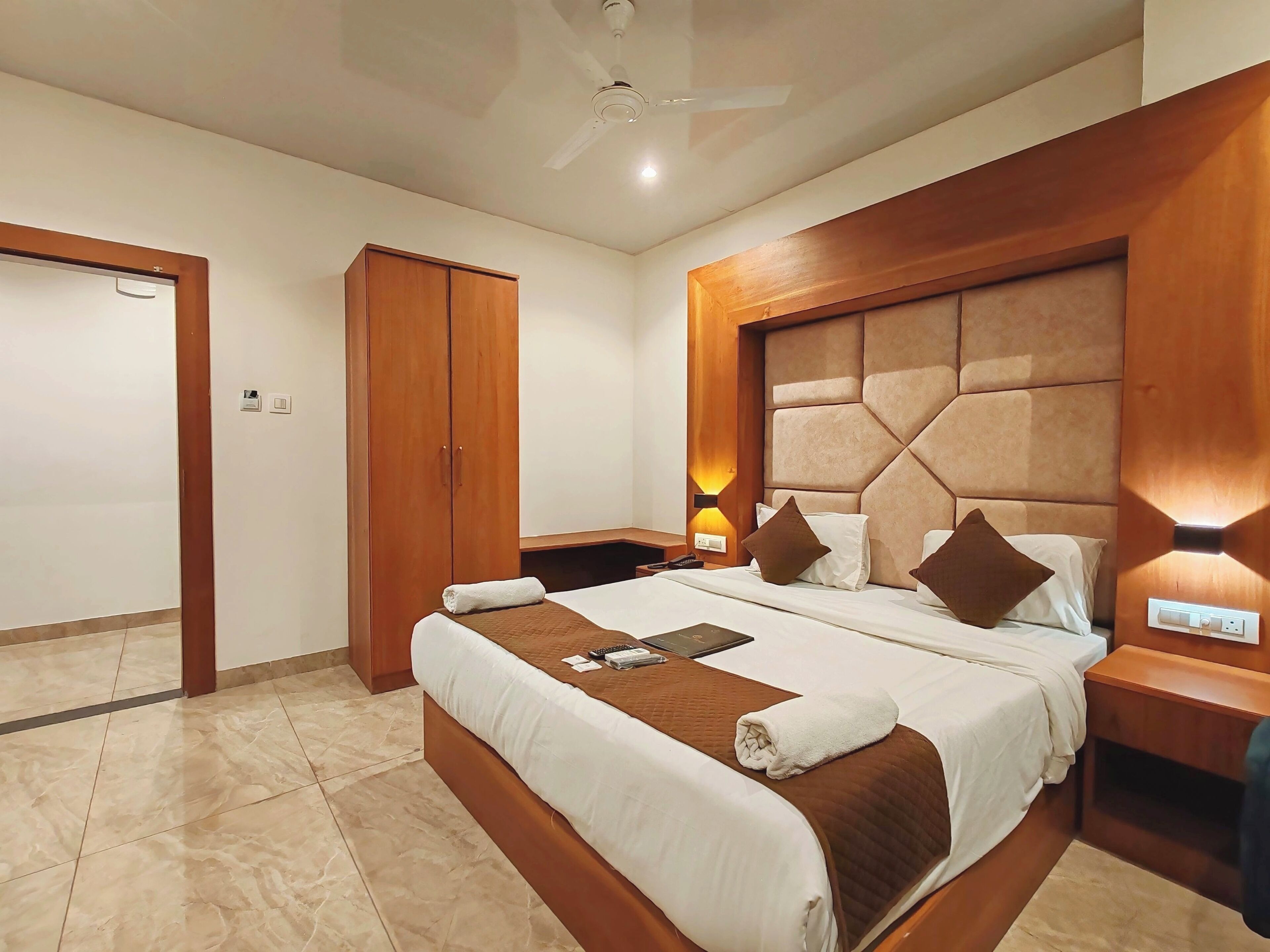 Una habitación de hotel con una cama grande, cabecera de madera, lámparas de noche y un armario.