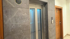 Un ascensore moderno con parete in marmo, porta in legno e indicatore del piano.