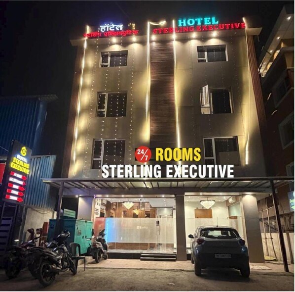 A hotel building with multiple floors, a sign indicating 24/7 rooms, and a visible entrance. - Hotel Sterling Executive (Navi Mumbai)