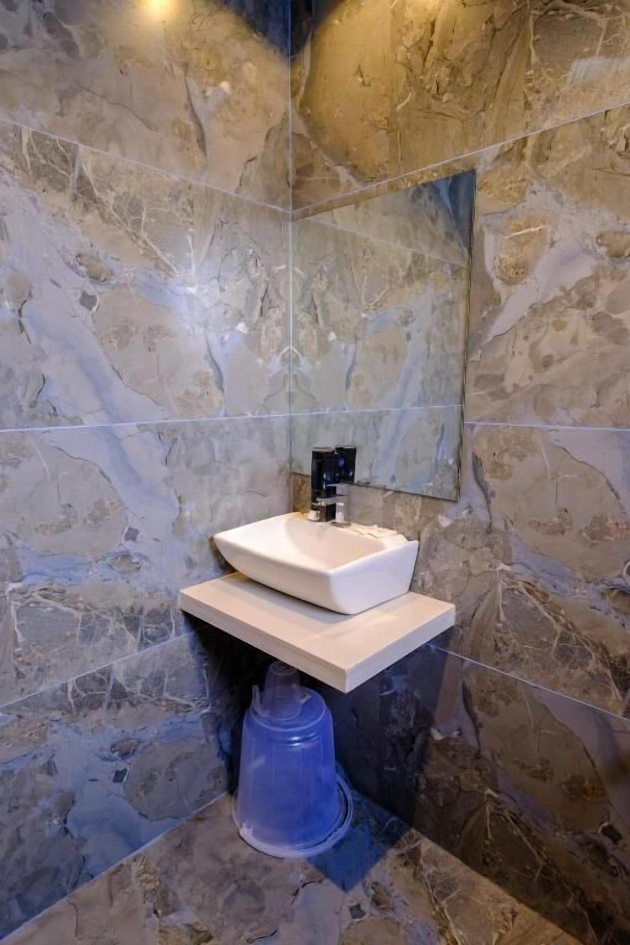 A bathroom with a marble wall, a white sink, and a mirror.