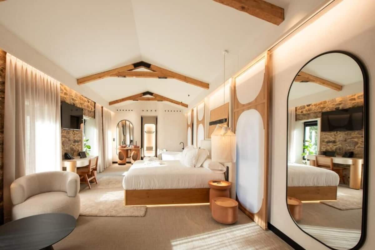 A modern bedroom with a large bed, a round mirror, a desk, and a chair.