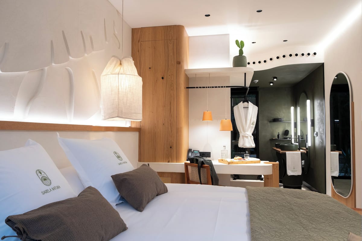 A modern hotel room with a large bed, a wooden headboard, a desk, and a bathroom.