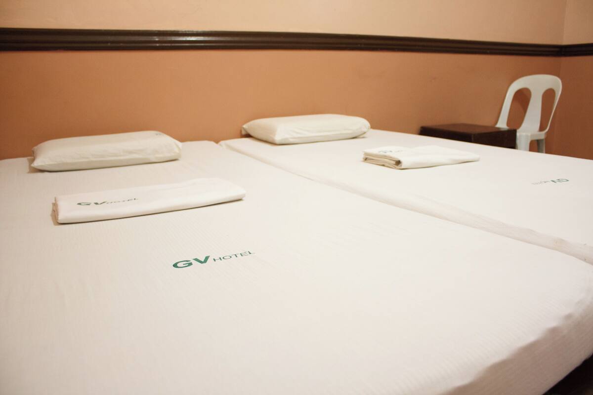 Ein Hotelzimmer mit zwei Betten, jeweils ausgestattet mit einem ordentlich gefalteten weißen Handtuch und einem Kissen.