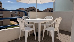 A balcony with a white table and chairs, a white umbrella, and a view of neighboring buildings. - Charming appartment La Pironnière - Les Sables - 4 people (Les Sables-d´Olonne)