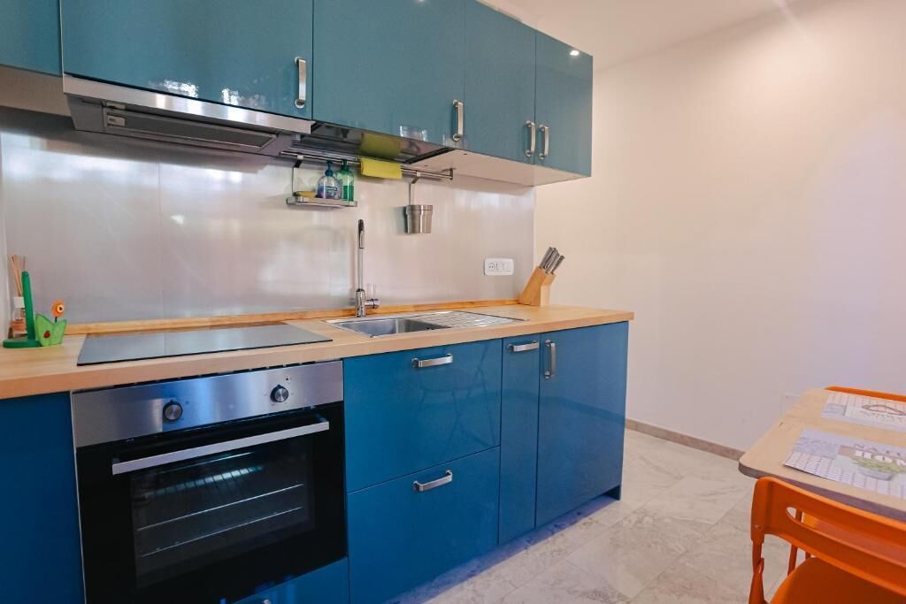 Una cocina con armarios azules, una campana extractora de acero inoxidable, un fregadero y un horno.
