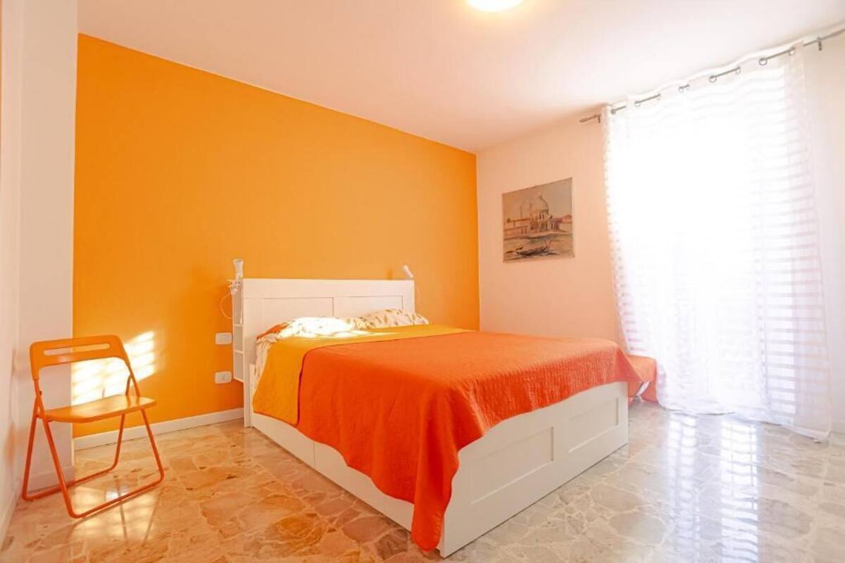 A bedroom with a bed, a chair, a painting on the wall, and a window with curtains.