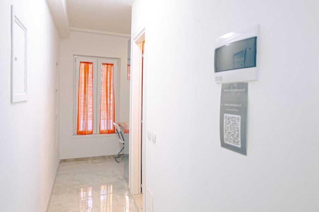 Un couloir avec une porte, une fenêtre ornée de rideaux orange, une chaise et un code QR sur le mur.