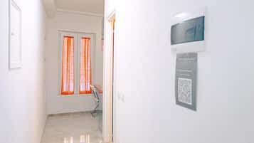 Un couloir avec une porte, une fenêtre ornée de rideaux orange, une chaise et un code QR sur le mur.