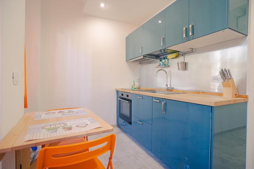 Une cuisine compacte avec des meubles de couleur turquoise, un plan de travail en bois et une petite table à manger avec des chaises orange.