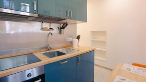 Una cucina compatta con mobili color petrolio, un lavello in acciaio inossidabile e un forno integrato.