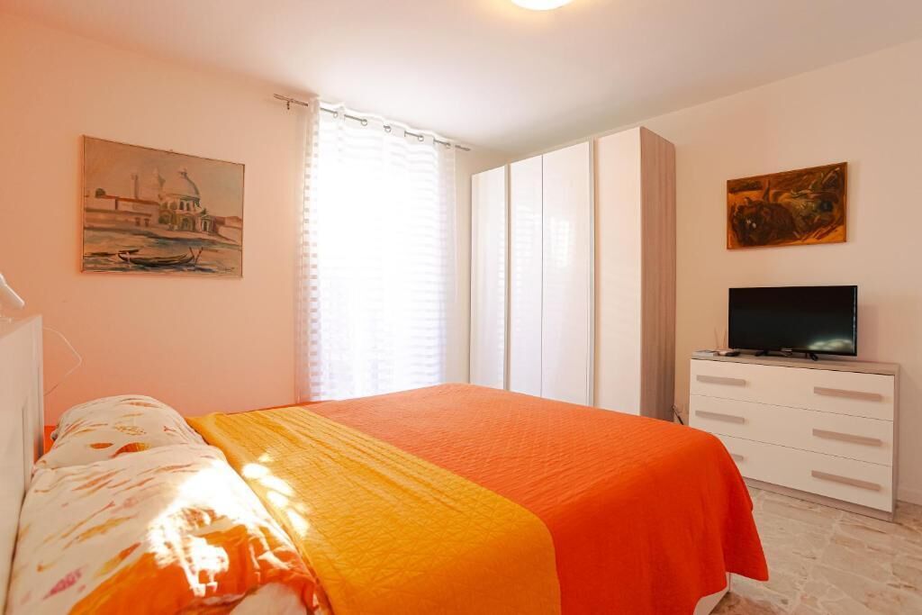 A bedroom with a bed, a television, a wardrobe, and a painting on the wall.