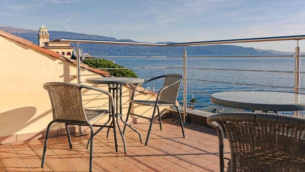 Una terrazza con posti a sedere all'aperto, vista sul mare e un edificio sullo sfondo.
