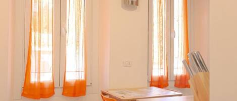 Une pièce avec une table et des chaises, une fenêtre avec des rideaux orange et un climatiseur fixé au mur.