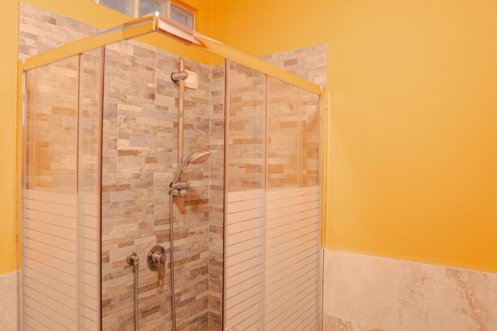 Ducha con cerramiento de vidrio, pared de azulejos, cabezal de ducha y una ducha de mano.