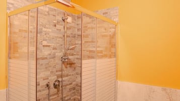 Ducha con cerramiento de vidrio, pared de azulejos, cabezal de ducha y una ducha de mano.