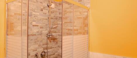 Ducha con cerramiento de vidrio, pared de azulejos, cabezal de ducha y una ducha de mano.