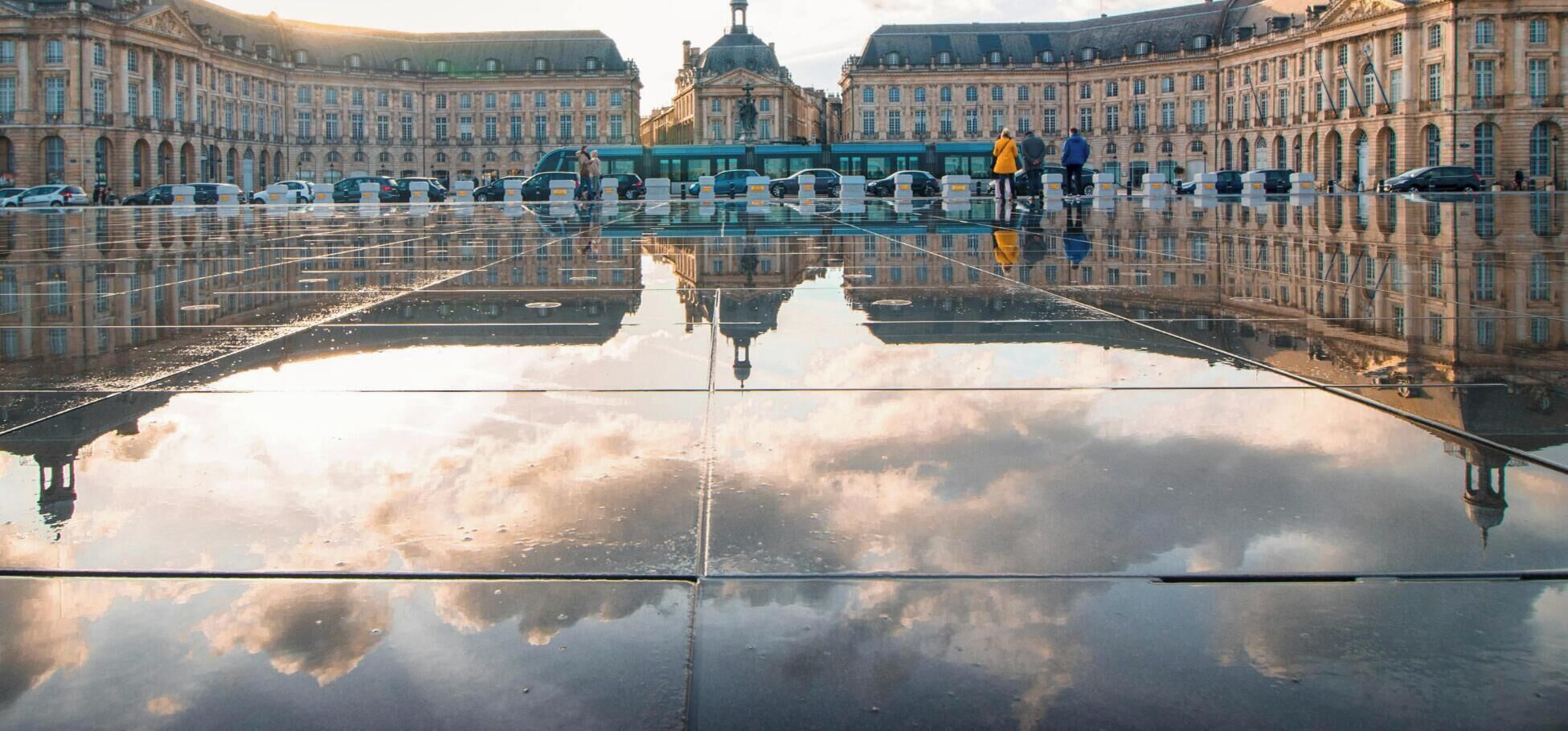 A large reflective plaza with classical architecture, a central monument, and a clear sky.