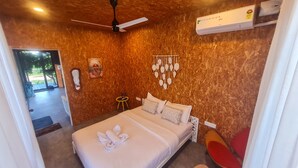 A hotel room with a bed, a ceiling fan, an air conditioning unit, and a small table with a chair. - Amram (Shoolagiri)