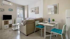 Ein gemütlicher Wohnbereich mit einer Couch, einem Fernseher, einem Esstisch mit Stühlen und einem Spiegel.