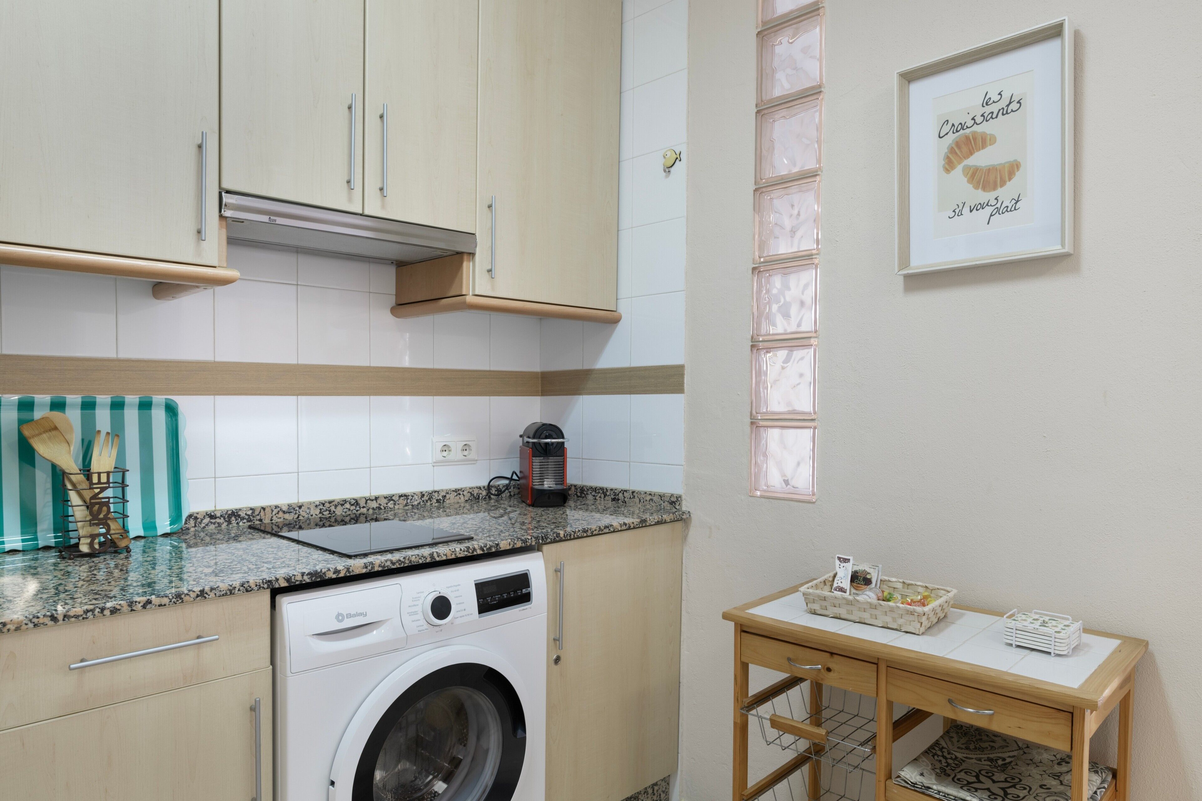 A kitchen with a washing machine, a countertop with a coffee maker, and a framed picture on the wall.