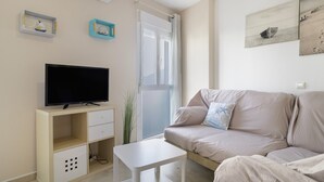 Ein Wohnzimmer mit Fernseher, einer Couch, einem kleinen Tisch und einem Fenster mit Vorhängen.