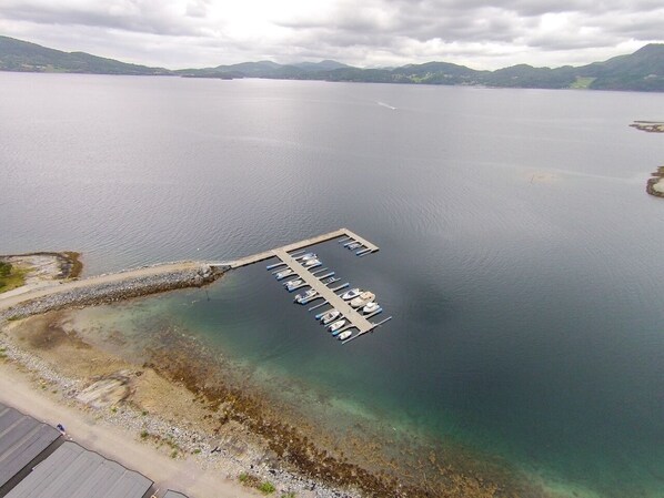 An aerial view of a calm lake with a dock extending into the water, surrounded by hills.