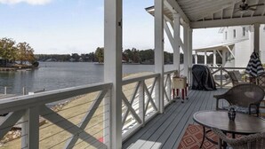 A covered deck with a view of a lake, a table with chairs, and a ceiling fan. - Lake Happy - Waterfront Paradise (Dadeville)