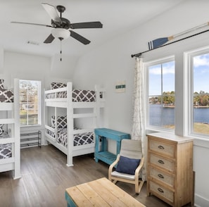 A room with bunk beds, a desk, a chair, a dresser, and a view of a body of water.