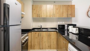 Een kleine keuken met houten kastjes, een roestvrijstalen koelkast, een magnetron en een broodrooster.