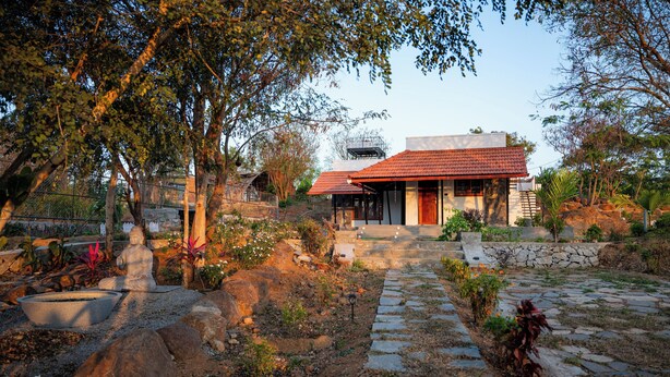 A house with a red-tiled roof, stone pathway, and surrounding vegetation. - Bodhi (Shoolagiri)