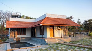 A modern house with a tiled roof, a swimming pool, and a stone-tiled patio. - Bodhi (Shoolagiri)