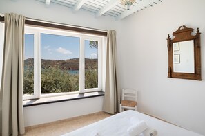 A bedroom with a large window, a bed, a chair, and a mirror on the wall. - House with stunning sea views in Agios Sostis (Μύκονος)